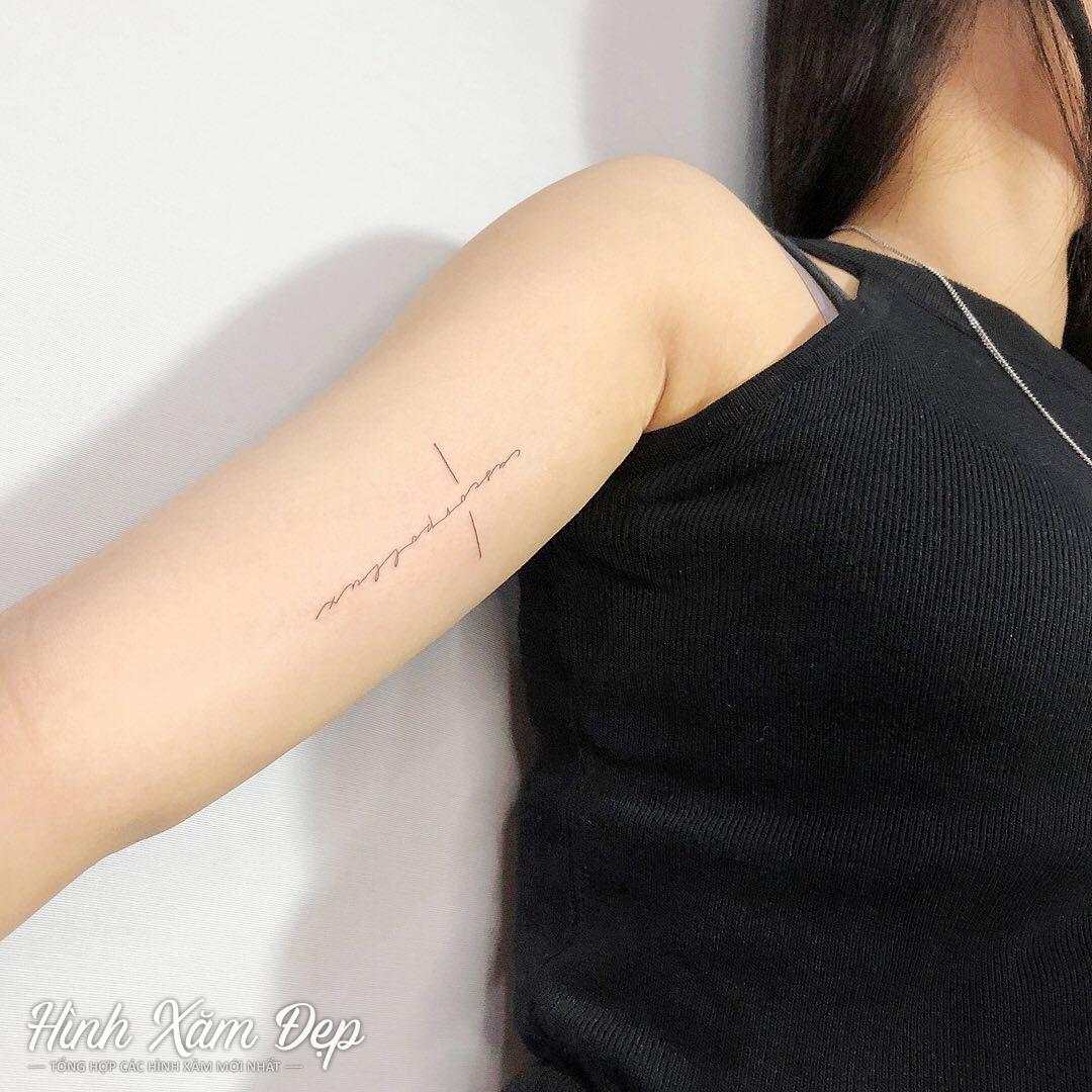 Hình xăm thánh giá chữ ở bắp tay nữ